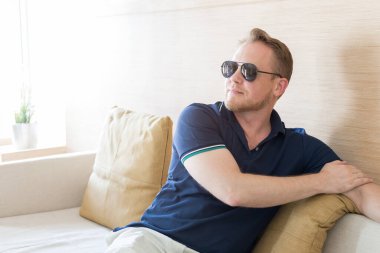 Genç beyaz adam güneş gözlüğü takıyor, kanepede dinleniyor..