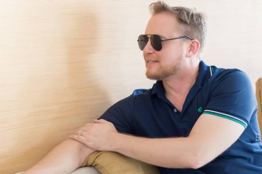 Genç beyaz adam güneş gözlüğü takıyor, kanepede dinleniyor..