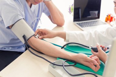 Steteskopla sfenometre kullanan bir doktor hastanede kan basıncını ölçüyor..