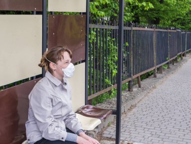 Güneşli bir bahar gününde, tıbbi solunum cihazına bağlı genç bir kadın otobüs durağında oturuyor. Coronavirus koruması. Açık havada..