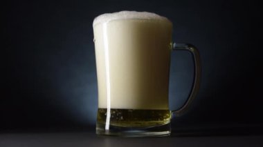 Bira damlaları dolup taşan bir bira bardağının kenarlarından aşağı akıyor. Yavaş çekim ve karanlık stil