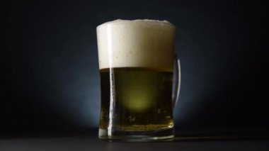 Dolu bir bira bardağı masada yavaşça döner. Yavaş çekim ve karanlık stil