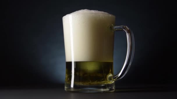 An overflowing beer mug slowly rotates on the table. Slow motion and dark style — Stock Video