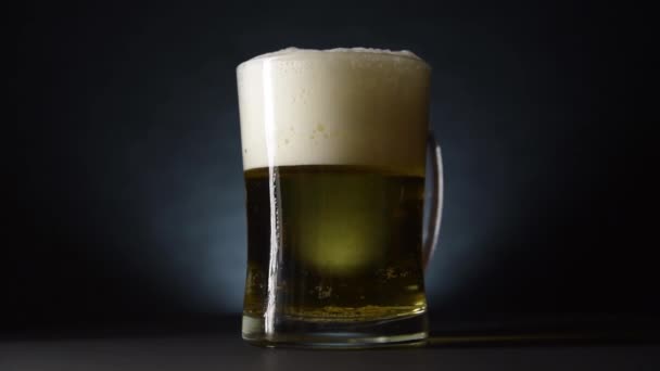 Una taza de cerveza desbordante gira lentamente sobre la mesa. Cámara lenta y estilo oscuro — Vídeos de Stock