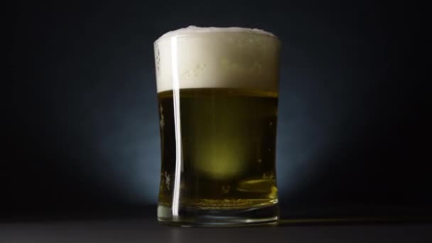 Uma caneca de cerveja transbordando gira lentamente sobre a mesa. Movimento lento e estilo escuro — Vídeo de Stock