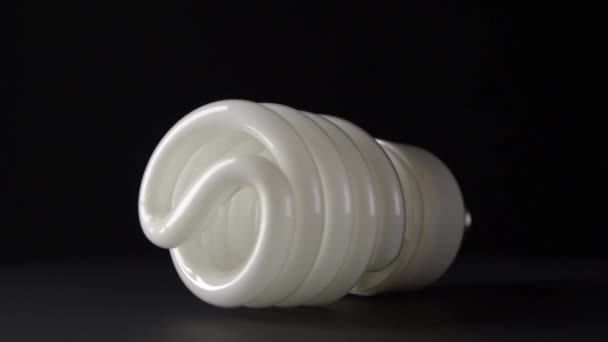 Witte energiebesparende lamp draait op een zwarte achtergrond — Stockvideo