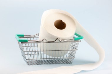 Tuvalet kağıdı mavi bir arka planda minyatür bir alışveriş arabasında yuvarlanıyor. Covid-19 salgını sırasında tuvalet kağıdı alma ve panik yapma kavramı..