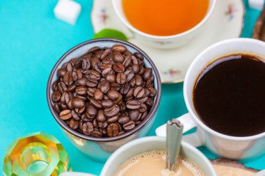 Çay ve kahve fincanı koleksiyonu, şeker küpleri ve kahve çekirdekleri, pastel mavi arka planda. Düz yatış, üst görünüm.