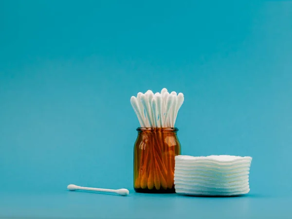 Q-tips, cotton swabs, cotton pads, isolated on bright blue background. Amber bottle