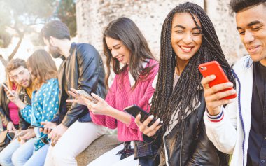 Multiracial group of teenagers have fun playing happily with smartphones. Use by millennials of cell phones and social applications. Focus on the face of a beauty mixed race girl with dreadlocks clipart