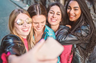Bir grup çok ırklı dört kız akıllı telefon yaşam tarzlarıyla selfie çekiyor. Kadın arkadaşlık yaşam tarzı konsepti. Mutlu çok ırklı milenyum öğrencileri birlikte hayatın tadını çıkarıyorlar..