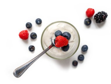 Böğürtlenli yoğurt dolu bir bardak ve saf beyaz arka planda izole edilmiş bir kaşık. Alan resminin sığ derinliği.
