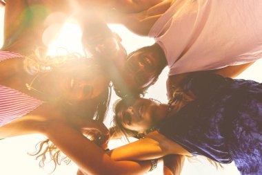 Yirmili yaşlarda bir grup genç kollarını bir çemberin içinde omuzlarına koyuyor. En iyi arkadaşlar yazın birbirlerini izleyerek eğleniyorlar. Güven ve dostluk kavramı. Alt görünüm.