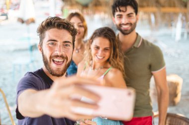 Yazın selfie çeken bir grup genç. Milenyumların en iyi arkadaşları sahilde eğleniyor. Fotoğrafları çeken sakallı genç adama odaklan. İnsanlar yeni teknoloji kavramını kullanıyor
