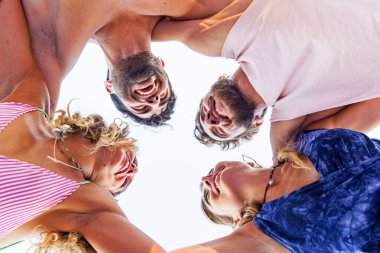 Yirmili yaşlarda bir grup genç kollarını bir çemberin içinde omuzlarına koyuyor. En iyi arkadaşlar yazın birbirlerini izleyerek eğleniyorlar. Güven ve dostluk kavramı. Alt görünüm.