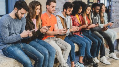 Gençlik, akıllı telefon ve sosyal medya ağlarına bağımlı. Genç insanlar bankta oturup kendi akıllı telefonlarını izliyorlar..