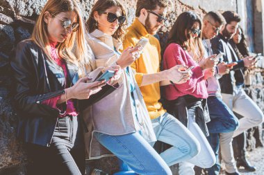 Milenyum kuşağı insanları akıllı telefon kullanıyor. Sosyal ağ bağımlılığı kavramına bağımlı gençler. Eski bir duvara karşı cep telefonu kullanan arkadaşlar. Orta bölüm.