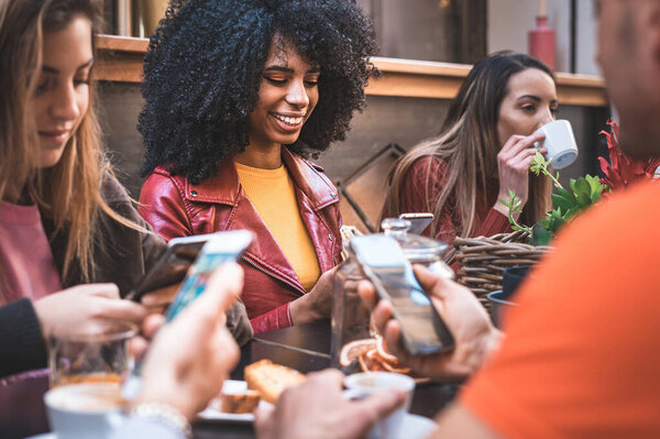 Group of young people sitting in a cafe and using social media application on smart phone. Young men and women meeting at cafe table using cell phone and always online. Focus on the african american woman with curly hair face