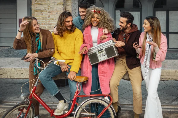 Multi racial group of people listening music from a vintage radio cassette player while theyre sitting on a urban bench. Integration from different young people. Youth lifestyle concept.