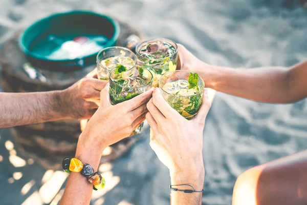 Best friends toasting with cocktails. Young people drinking at aperitif. Shallow depth of field with focus on friends hand clinking with juice glass. Close up of hands, friendship lifestyle concept