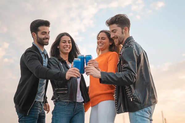 İki erkek ve iki kız dışarıda bira kutusuyla gülüp kadeh kaldırıyorlar. Tasasız gençlik dışarıda eğleniyor..