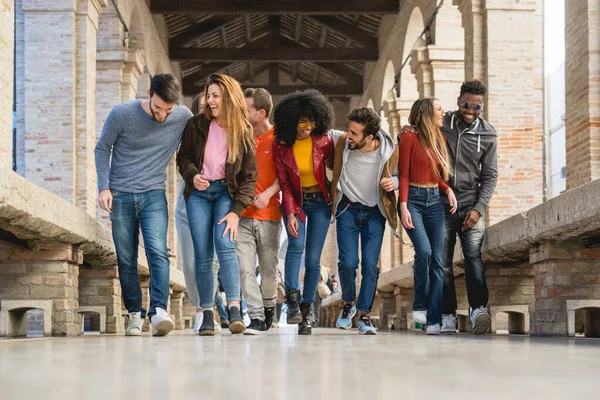 Group of trendy young people chatting together standing on a wall outdoors. Students having fun together. Focus on on the blonde girl smiling. Lifestyle concept.