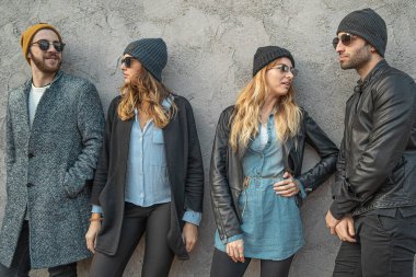 Bir grup modaya uygun genç kadın ve erkek beton desenli duvarın önünde dikilip birlikte eğleniyorlar.