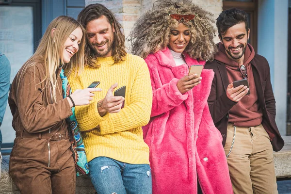 Group of interracial best friends using smartphone standing outdoor in the city. Young people having fun using smartphone, the internet and social media application.