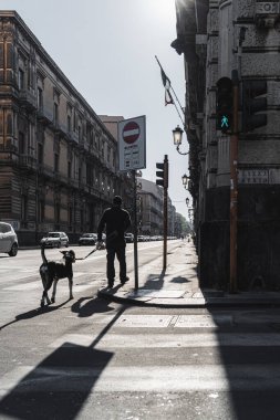 Catania, Sicilya / İtalya - 04-11-2020 Coronavirus (Covid-19) karantina döneminde bir kişi, köpeğinin üzerinden geçerek Catania 'nın ıssız sokaklarında yürür.