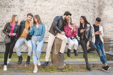 Karışık ırk insanları birlikte konuşarak ve dışarıda akıllı telefonlarını kullanarak eğleniyorlar. Boş zaman aktiviteleri yaşam tarzı konsepti