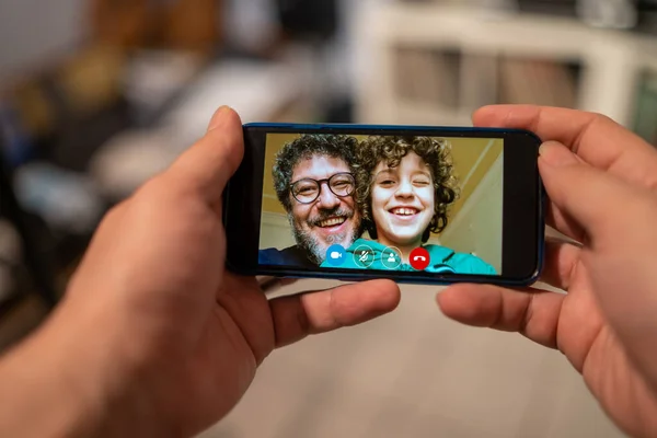 Baba ve oğul, koronavirüs salgını nedeniyle karantinadayken akrabalarına akıllı telefon görüşmeleri yapıyorlar. İnsanlar teknolojiyi güvende kalmak ve ailelerine yakın olmak için kullanıyorlar..