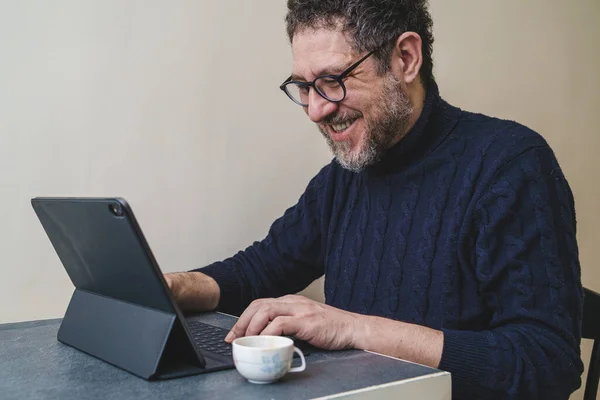 Volwassen Man Alleen Thuis Glimlachend Met Een Tablet Koffie Drinkend — Stockfoto