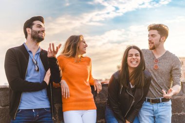 Bir grup modaya uygun genç, açık havada küçük bir duvarın üzerinde sohbet ediyorlar. Öğrenciler birlikte eğleniyor ve ağzı açık gülüyorlar. Gençliğin eğlenceli konsepti.