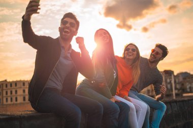 Gün batımında dışarıda bir bankta selfie çeken mutlu gençler. Gerçek bir ışık patlaması. Boş zaman aktiviteleri yaşam tarzı konsepti.