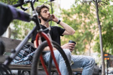 Hippi adam kenarda oturup Amerikan kahvesi içiyor ve kulaklıkla müzik dinliyor..