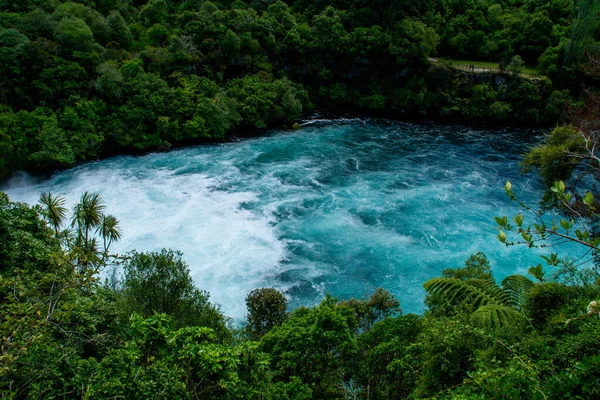 Travel New Zealand. Most popular tourist attraction Huka Falls at Lake Taupo, North Island. White and turquoise water, green forest on background. Beautiful landscape view. Active summer holidays.