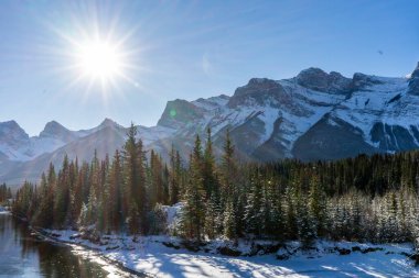 Kanada Peyzajı. Karla kaplı dağ manzarası, Bow Nehri ve kışın Üç Kız Kardeş manzarası. Kanada dağlarında güneşli güzel bir gün. Canmore, Alberta, Kanada.