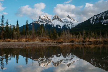 Gün batımında Polis Deresi 'nin sakin sularında üç kız kardeşin ikonik dağ tepelerinin nefes kesen görüntüsü. Canmore, Alberta, Kanada.