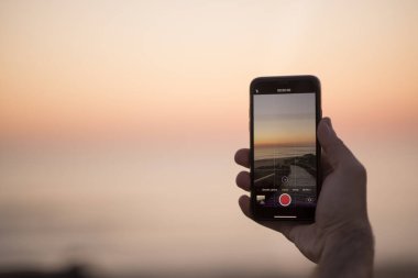Telefon gün batımında sahilde fotoğraf çekiyor.