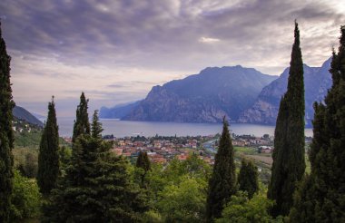 Kuzey Lago di Garda (Garda Gölü), Trentino, İtalya 'da Torbole' un dramatik bulutlu gökyüzü ile panoramik akşam gün batımı manzarası; Corona Virüs Salgını 'nın boş otel odaları yüzünden turizmde yaşanan mali kayıp