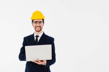 Akıllı genç mimar gözlük takıyor ve planlanan işi kontrol etmek için elinde dizüstü bilgisayar tutan sarı kasklı. Pankart için resim beyazından izole edilmiş arkaplan.