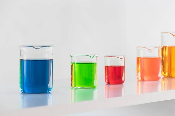 在科学实验室的白色背景上的玻璃杯烧杯中的五颜六色溶液 — 图库照片