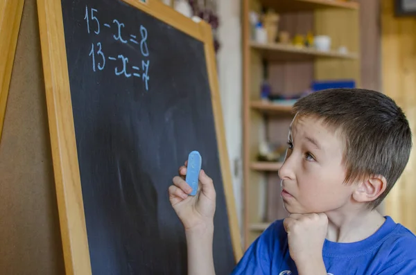 The boy at the blackboard was thinking about a math problem.