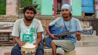 Varanasi şehrinde Ganj Nehri 'nin kıyısında gitar ve davul çalan iki sokak müzisyeni Hint mantraları söylüyor..