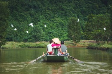 Ninh Binh Vietnam 'da. Tam Coc nehrinde bir tekne. Kuşlar uçuşuyor. Hayvanlar için vahşi yaşam cenneti. Bir teknede rehber taşıyan turistler.