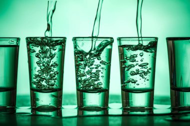 Su yeşil arka planda küçük bardaklara dökülüyor