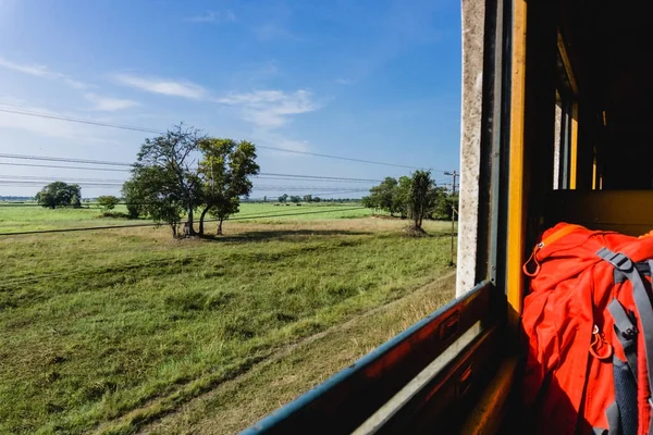 Open window train travel. Sunny summer in Thailand. Travelling with big backpack. Through the window landscape.