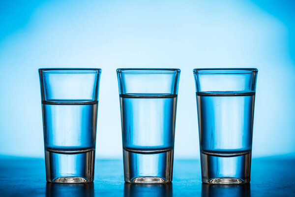 Three shots filled with transparent liquid on a blue background.