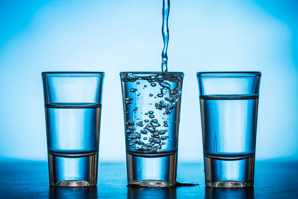 water being poured into small glasses on blue background