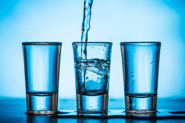 water being poured into small glasses on blue background
